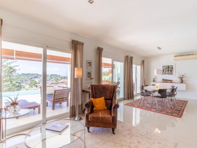 Salón-comedor diáfano con amplios ventanales que conectan directamente con la terraza, piscina y vistas al paisaje. Suelos de gres blanco y mobiliario contemporáneo.