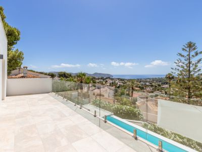 Terraza exterior con suelo de gres claro y barandilla de cristal. Vistas panorámicas al mar Mediterráneo, la bahía y el entorno urbano, incluyendo una piscina alargada y vegetación.