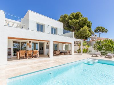 Villa moderna con piscina de azulejos claros y amplias terrazas. Cuenta con comedor exterior cubierto, zona lounge y barandillas de cristal en la planta superior.