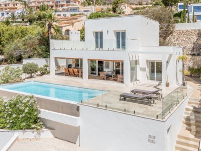 Villa moderna de dos plantas con piscina de borde infinito y amplias terrazas. Incluye zona de comedor exterior cubierta y solárium con tumbonas.