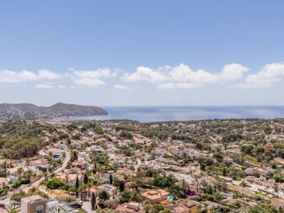 Vista panorámica de una zona residencial costera, con tejados de terracota, abundante vegetación y el mar Mediterráneo extendiéndose hasta el horizonte.