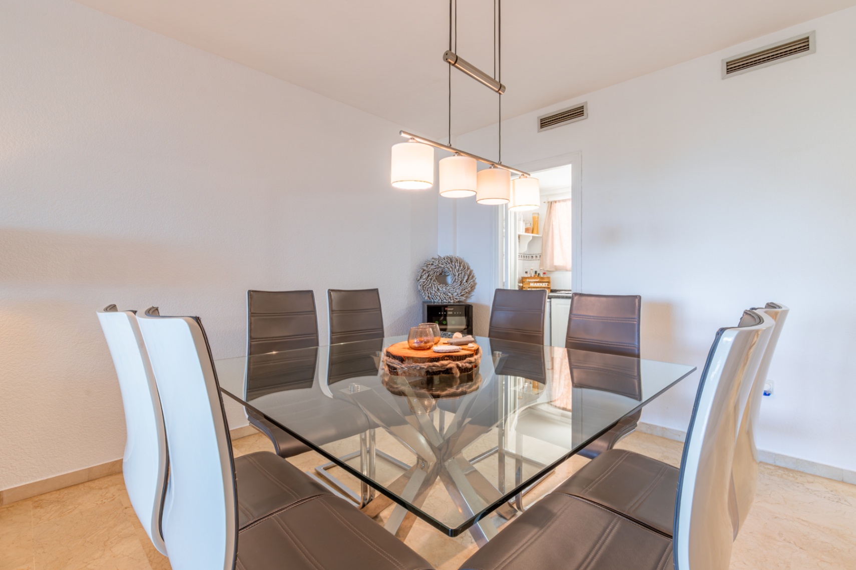 Comedor con mesa cuadrada de cristal y base metálica, rodeada de sillas de cuero. Una lámpara colgante moderna ilumina el espacio, que conecta con la cocina. Comedor con mesa cuadrada de cristal y base metálica, rodeada de sillas de cuero. Una lámpara colgante moderna ilumina el espacio, que conecta con la cocina.