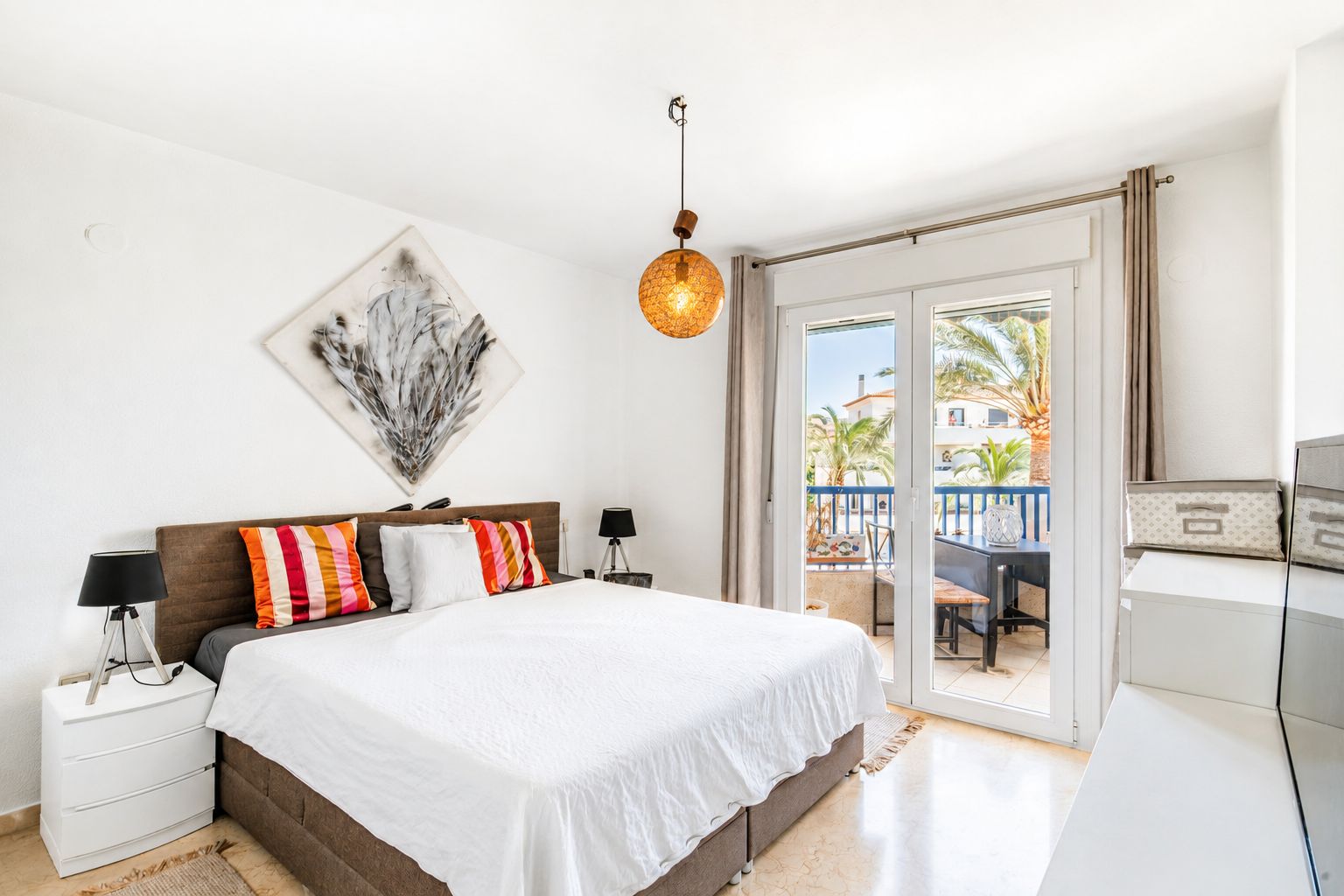 Dormitorio principal luminoso con acceso directo a una terraza privada, suelo de mármol y vistas a palmeras. Destaca su lámpara colgante y arte abstracto. Dormitorio principal luminoso con acceso directo a una terraza privada, suelo de mármol y vistas a palmeras. Destaca su lámpara colgante y arte abstracto.