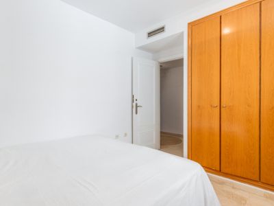 Dormitorio secundario con amplio armario empotrado de madera clara y cama con ropa blanca. Destaca el suelo de mármol y la puerta abierta que conecta a otra estancia.