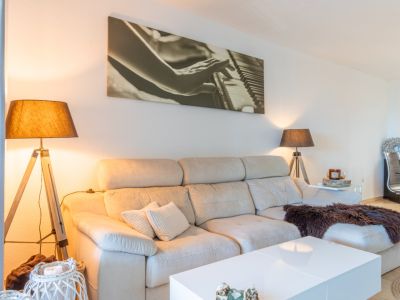 Salón con sofá seccional claro, mesa de centro blanca y dos lámparas de pie de diseño. Un gran cuadro de piano decora la pared, creando un ambiente acogedor.