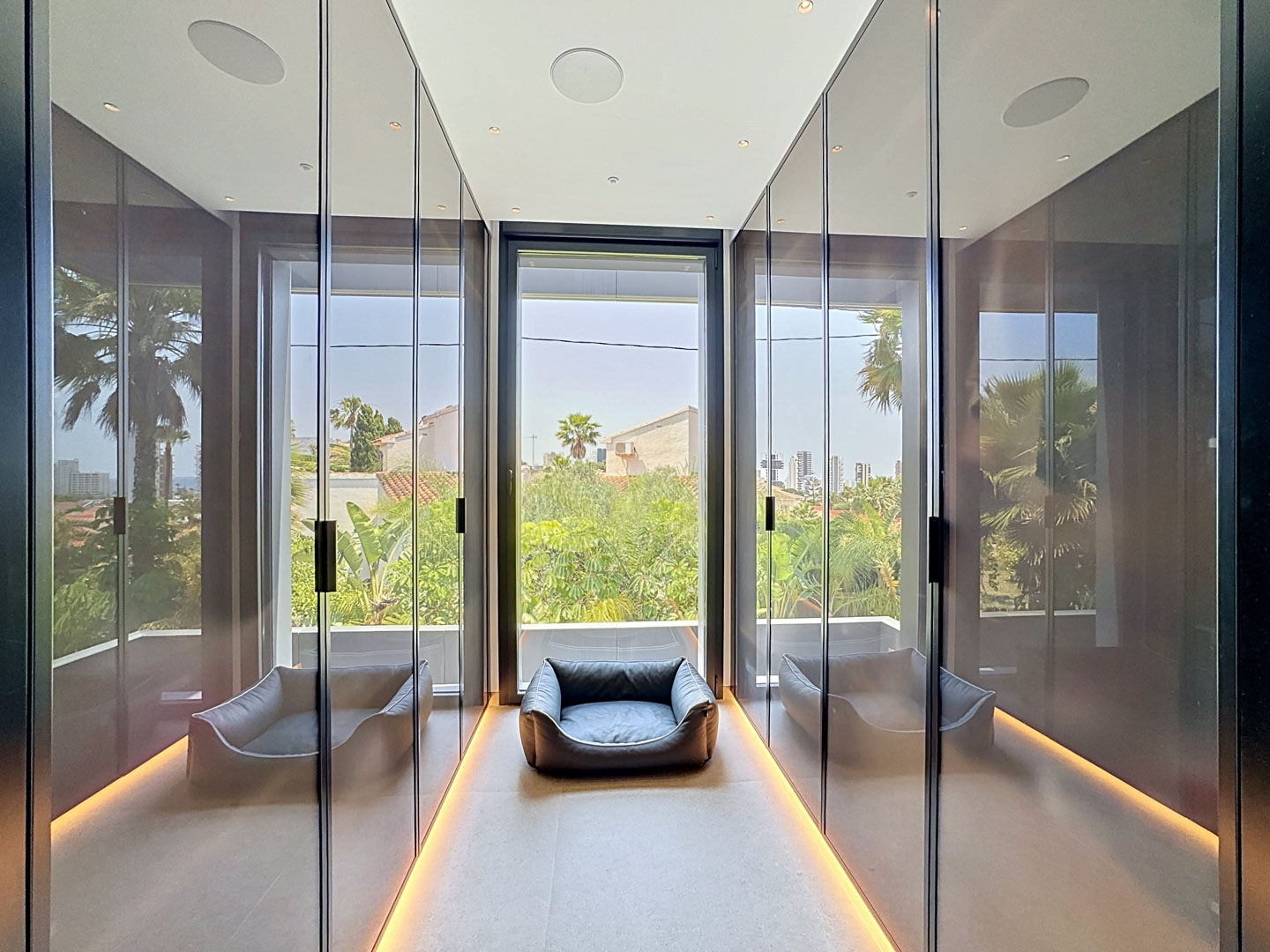 Elegante vestidor con armarios de espejo de suelo a techo, iluminación ambiental de suelo y gran ventanal con vistas a la vegetación tropical.