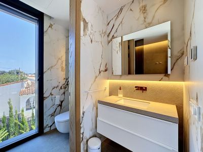 Baño de diseño con revestimiento mural de mármol veteado y un gran ventanal que ofrece vistas residenciales. Incluye tocador flotante con encimera texturizada y grifería empotrada.
