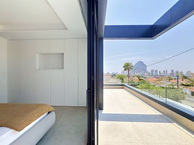 Dormitorio con armarios empotrados blancos y cama moderna, con acceso directo a una terraza exterior. Disfruta de vistas panorámicas a Calpe y al majestuoso Peñón de Ifach.