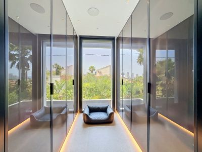 Elegante vestidor con armarios de espejo de suelo a techo, iluminación ambiental de suelo y gran ventanal con vistas a la vegetación tropical.