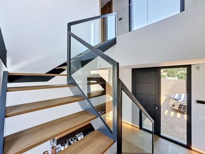 Escalera flotante contemporánea con peldaños de madera de roble y barandilla de cristal, iluminada por luz natural en un vestíbulo de doble altura.