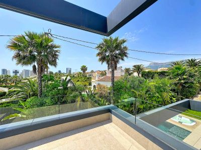 Terraza superior con suelo de gres y barandilla de cristal, ofreciendo vistas panorámicas a la exuberante vegetación, la ciudad y las montañas, con la piscina y jacuzzi integrados abajo.