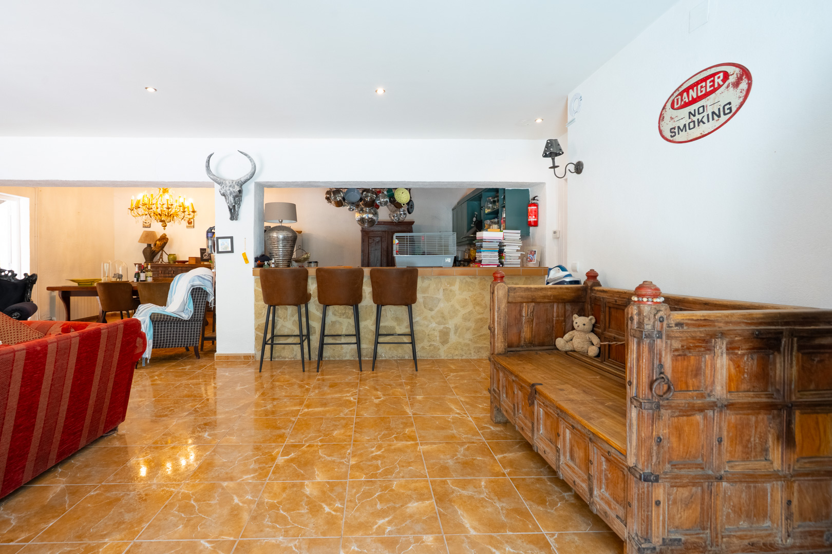 Amplia sala de estar con barra de piedra y taburetes de cuero, conectada a la cocina y comedor. Destacan los suelos de baldosas brillantes y el banco de madera tallada. Amplia sala de estar con barra de piedra y taburetes de cuero, conectada a la cocina y comedor. Destacan los suelos de baldosas brillantes y el banco de madera tallada.