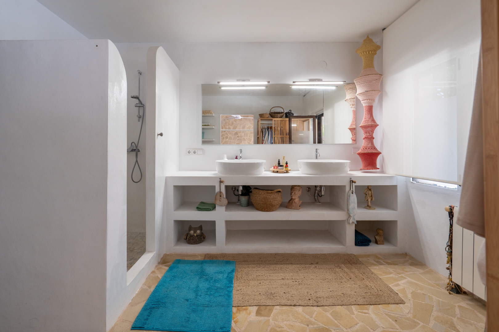 Amplio baño con doble lavabo integrado en encimera blanca, ducha de obra con pared curva y suelo de baldosas de piedra irregular. Espejo con iluminación. Amplio baño con doble lavabo integrado en encimera blanca, ducha de obra con pared curva y suelo de baldosas de piedra irregular. Espejo con iluminación.