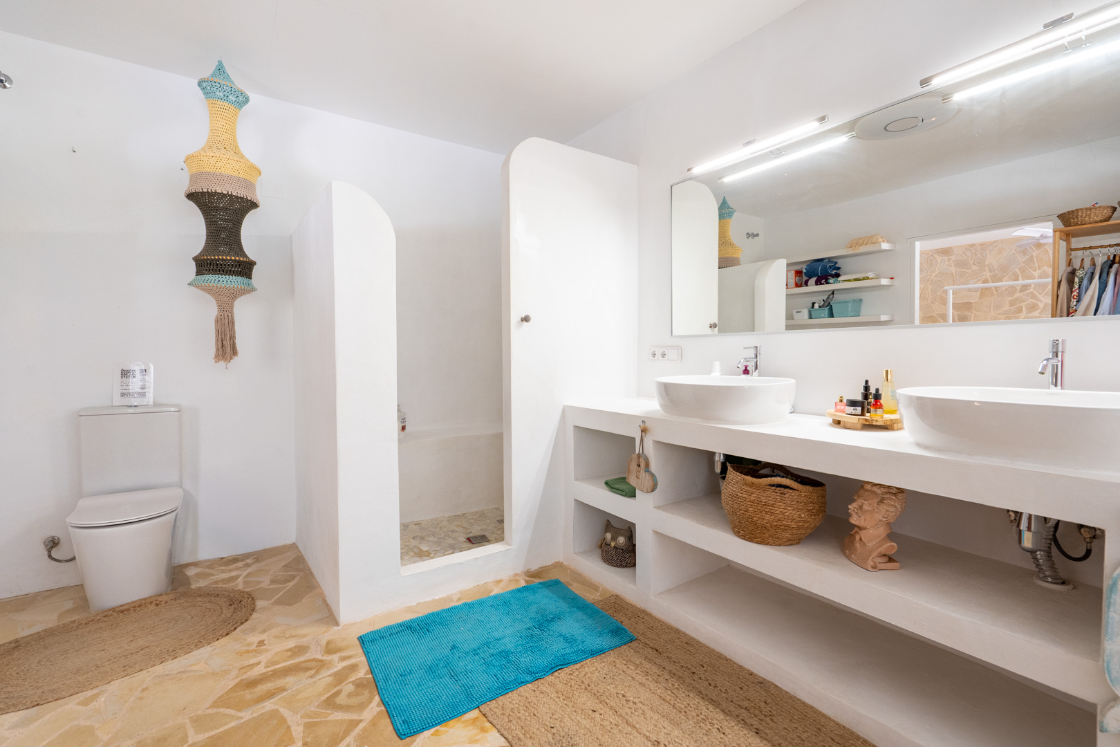 Baño luminoso con doble lavabo sobre encimera, ducha abierta con suelo de piedra irregular y paredes blancas. Destaca una lámpara colgante textil y el suelo de baldosas de piedra natural. Baño luminoso con doble lavabo sobre encimera, ducha abierta con suelo de piedra irregular y paredes blancas. Destaca una lámpara colgante textil y el suelo de baldosas de piedra natural.