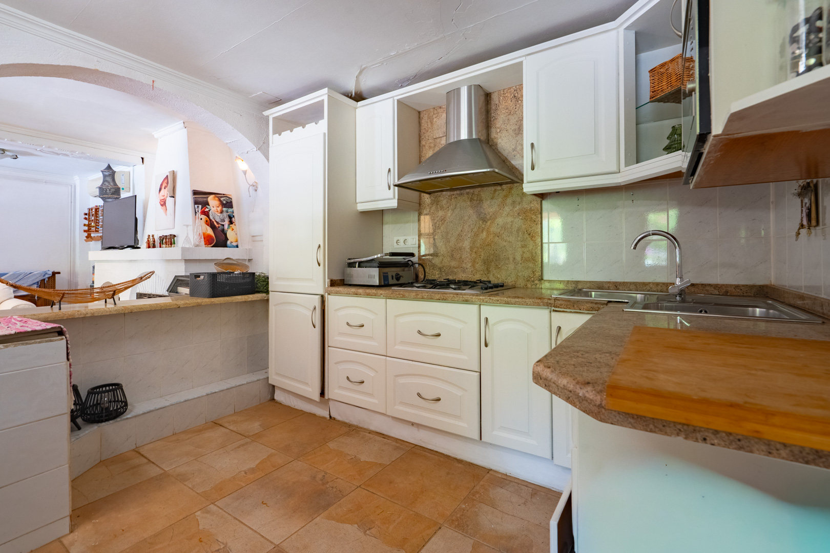 Cocina semiabierta con armarios blancos tradicionales, encimeras de granito y placa de gas. Dispone de fregadero doble y suelo de baldosas de terracota que conecta con una barra. Cocina semiabierta con armarios blancos tradicionales, encimeras de granito y placa de gas. Dispone de fregadero doble y suelo de baldosas de terracota que conecta con una barra.