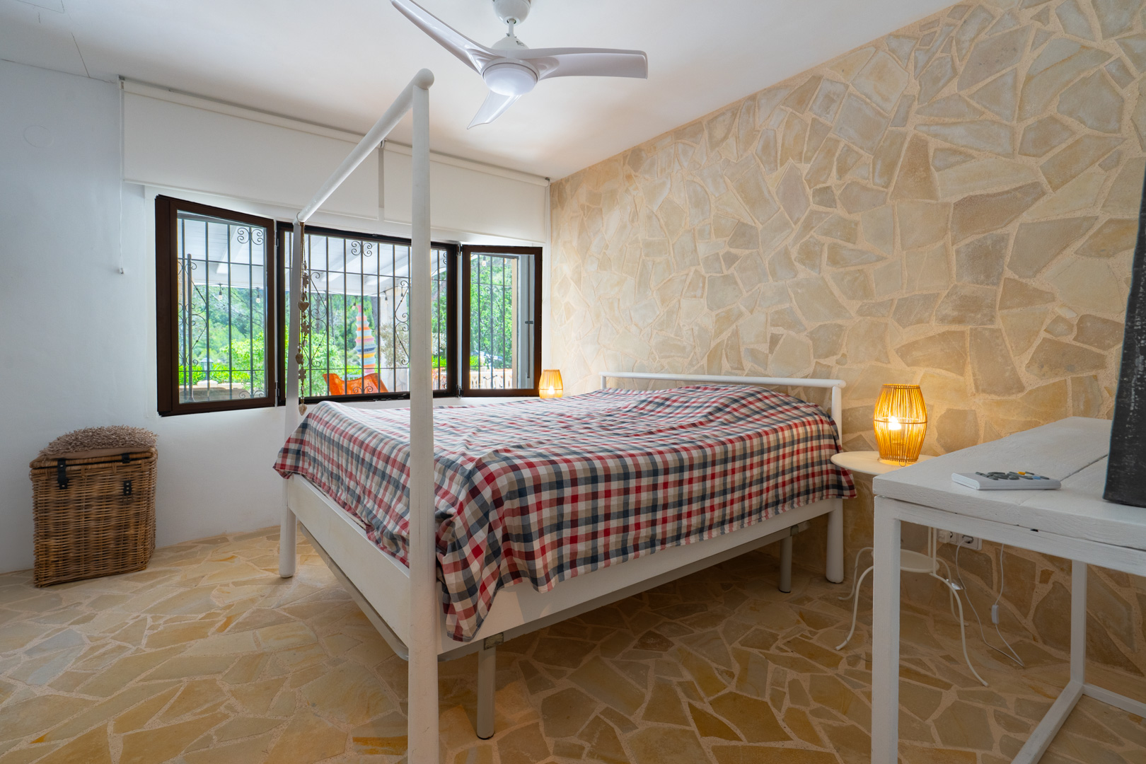Dormitorio con cama con dosel, pared de acento y suelo de piedra irregular, y ventanas con rejas que ofrecen vistas a la vegetación exterior. Dormitorio con cama con dosel, pared de acento y suelo de piedra irregular, y ventanas con rejas que ofrecen vistas a la vegetación exterior.