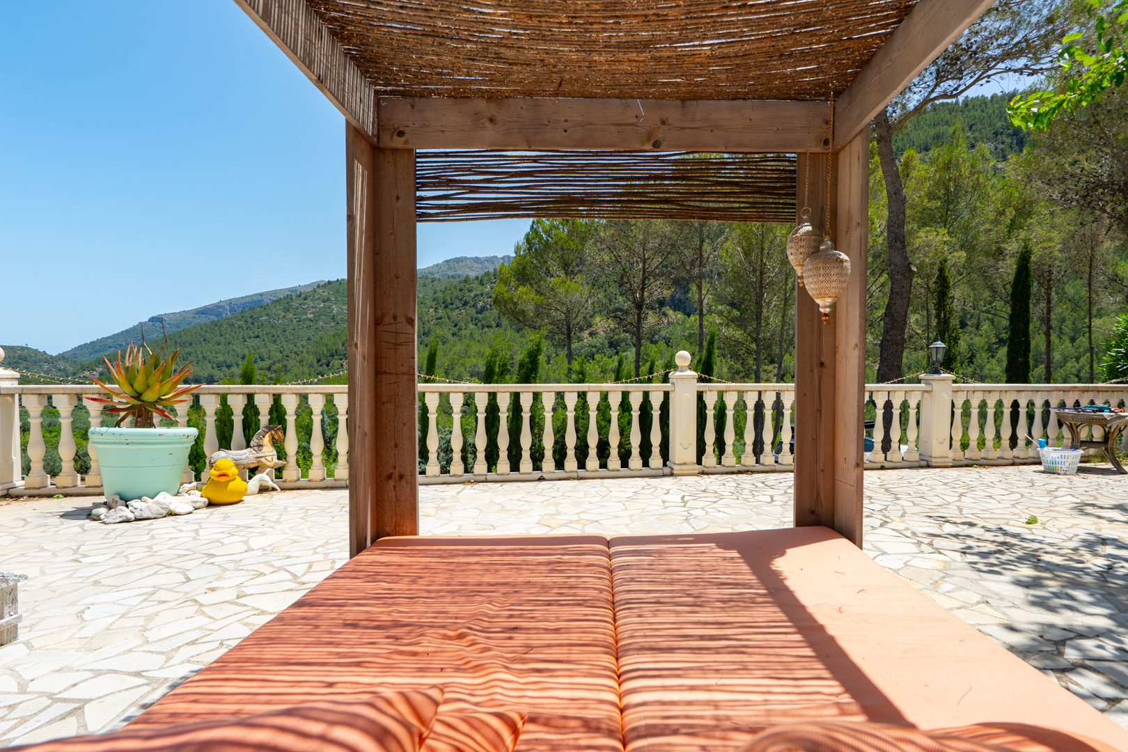 Espaciosa terraza exterior con pérgola de madera y techo de paja, cubriendo una doble tumbona. Ofrece vistas panorámicas a las montañas y está delimitada por una balaustrada clásica. Espaciosa terraza exterior con pérgola de madera y techo de paja, cubriendo una doble tumbona. Ofrece vistas panorámicas a las montañas y está delimitada por una balaustrada clásica.