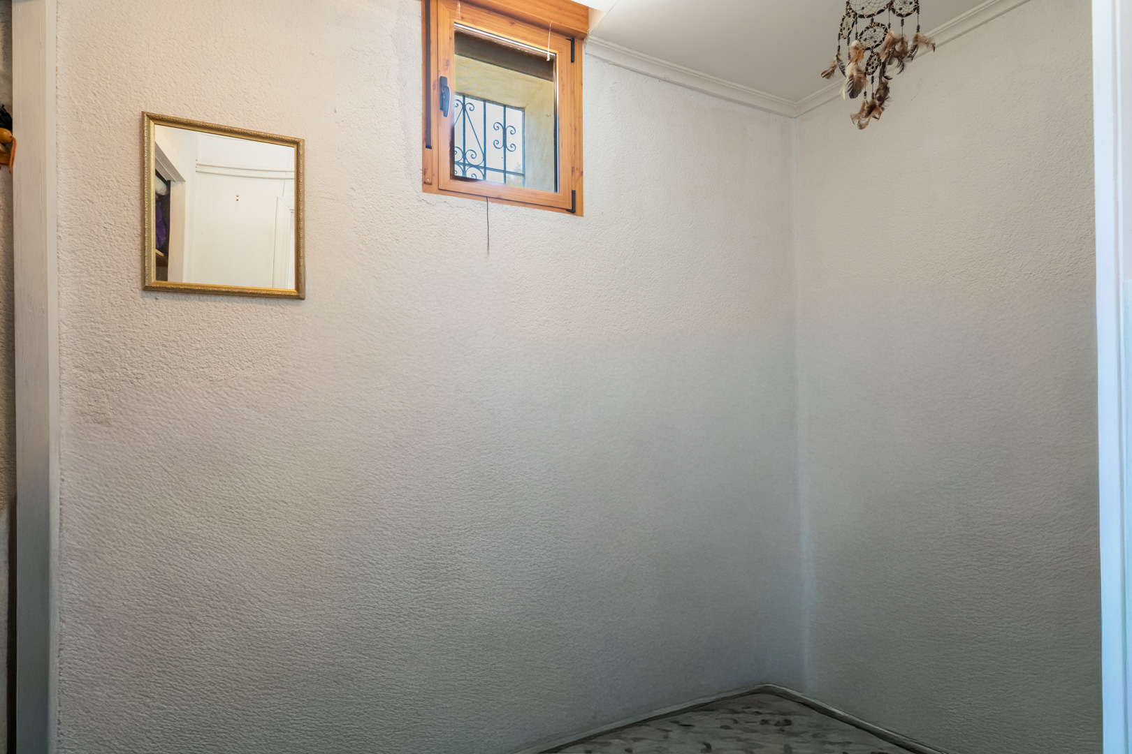 Pequeño dormitorio o alcoba con ventana de madera y rejas, que aporta luz natural. Un espejo con marco dorado y una decoración cuelgan de las paredes texturizadas. Pequeño dormitorio o alcoba con ventana de madera y rejas, que aporta luz natural. Un espejo con marco dorado y una decoración cuelgan de las paredes texturizadas.