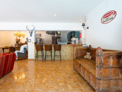 Amplia sala de estar con barra de piedra y taburetes de cuero, conectada a la cocina y comedor. Destacan los suelos de baldosas brillantes y el banco de madera tallada.