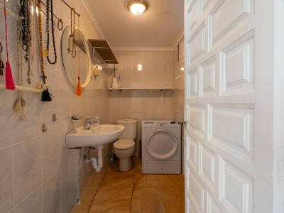 Baño funcional con azulejos claros, suelo de terracota y puerta panelada blanca. Incluye lavabo, inodoro y lavadora, optimizando el espacio.