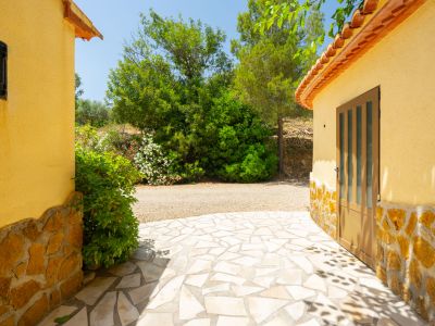 Patio exterior con pavimento de piedra irregular, flanqueado por dos edificios de estuco amarillo con zócalo de piedra y rodeado de vegetación.