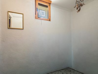 Pequeño dormitorio o alcoba con ventana de madera y rejas, que aporta luz natural. Un espejo con marco dorado y una decoración cuelgan de las paredes texturizadas.