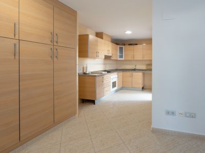 Amplia cocina con armarios de madera clara, encimeras de granito moteado y horno integrado. Un gran mueble despensero a juego se sitúa a la izquierda sobre el suelo de baldosas beige.