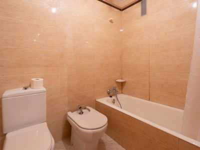 Baño con paredes de azulejos beige, equipado con inodoro, bidé y bañera con cortina. Incluye grifería cromada y estante esquinero.