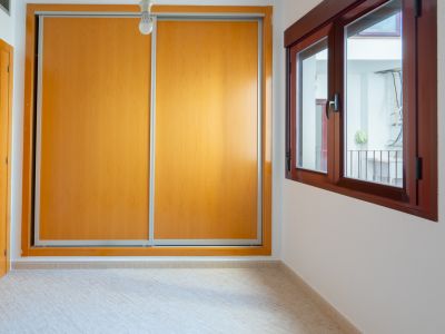 Dormitorio secundario con amplio armario empotrado de puertas correderas de madera clara y ventana de madera oscura con vistas a un patio interior.