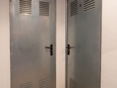 Dos puertas metálicas grises con ventilación superior e inferior, una marcada con 'Benissa Denia' y la otra con el número '5', sobre un suelo de granito moteado.