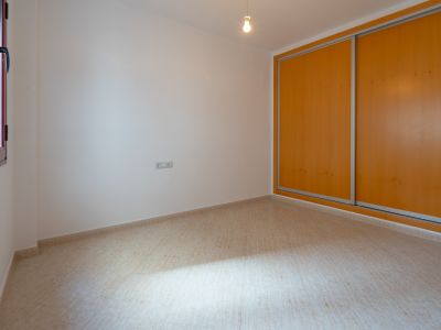 Habitación luminosa con suelo de gres beige y paredes blancas. Incluye un armario empotrado de dos puertas correderas de madera clara y una ventana con marco oscuro que aporta luz natural.