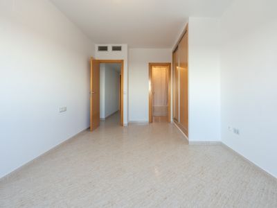 Habitación vacía con suelo de baldosas claras, armario empotrado de madera y puertas que conectan a otras estancias. Se aprecian rejillas de aire acondicionado.