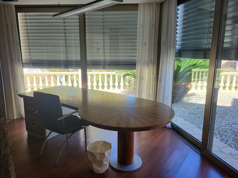 Amplio despacho privado con suelo de madera. Grandes ventanales ofrecen vistas al exterior con balaustrada y jardín mediterráneo.