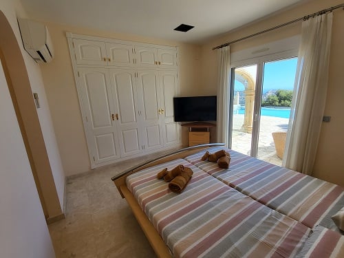 Dormitorio con dos camas individuales, armario empotrado y acceso directo a la piscina. Equipado con TV y aire acondicionado, ofrece vistas al exterior.