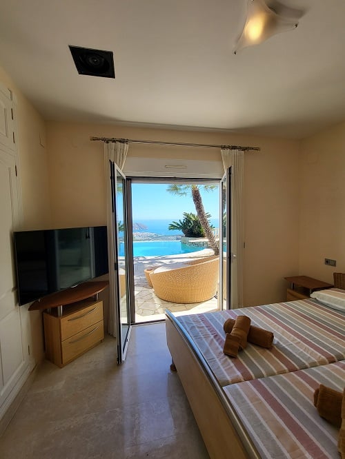 Dormitorio luminoso con acceso directo a la terraza, ofreciendo vistas panorámicas a la piscina infinity y al mar. Incluye camas individuales, televisor y suelos de mármol.