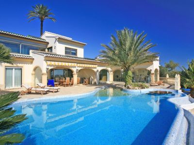 Amplia piscina de mosaico azul con entrada tipo playa, isla de palmeras y mesa acuática. La villa ofrece una naya cubierta y un gimnasio acristalado.