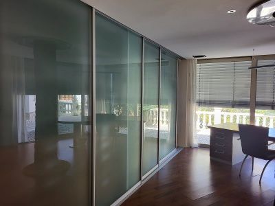 Despacho o dormitorio con elegantes puertas correderas de cristal esmerilado, suelo de madera oscura y zona de trabajo junto a la ventana con vistas a la balaustrada.