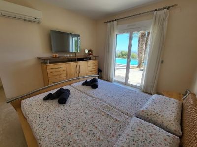 Dormitorio con camas individuales, TV y acceso directo a la terraza con piscina y vistas a las palmeras. Climatización y mobiliario de madera.