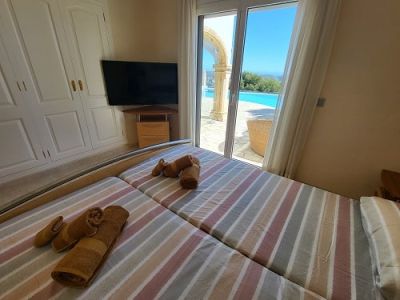 Dormitorio con dos camas individuales, armario empotrado y televisor. Acceso directo a la zona exterior de la piscina con un arco y vistas despejadas.