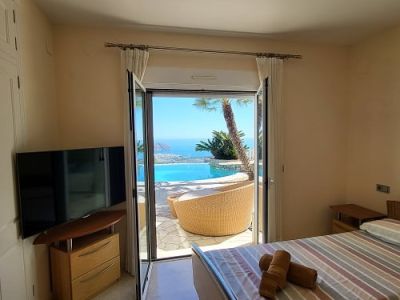 Dormitorio luminoso con acceso directo a la terraza, ofreciendo vistas panorámicas a la piscina infinity y al mar. Incluye camas individuales, televisor y suelos de mármol.