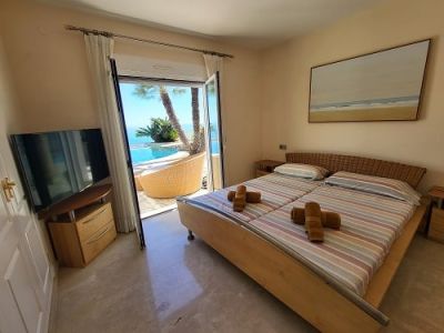 Dormitorio luminoso con camas individuales y cabecero de mimbre, ofreciendo acceso directo a la piscina y vistas al mar. Incluye televisor y arte mural.