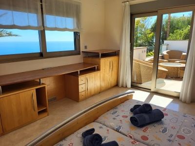 Dormitorio luminoso con dos camas individuales, escritorio de madera integrado y amplias vistas al mar. Acceso directo a una terraza privada con mobiliario exterior.