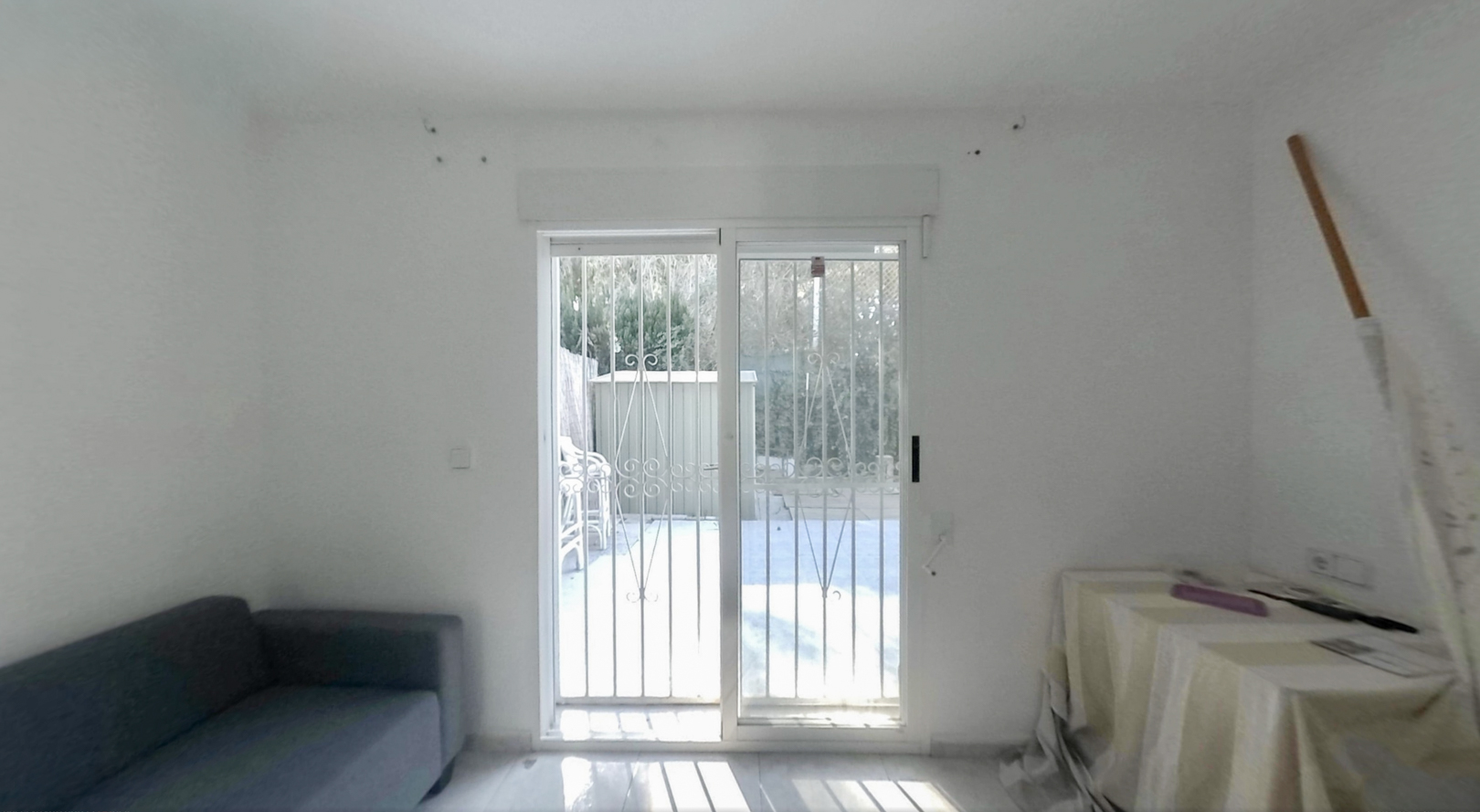 Amplia estancia con puertas correderas de cristal y rejas de seguridad, ofreciendo acceso directo al jardín privado e iluminada por luz natural sobre el suelo claro.