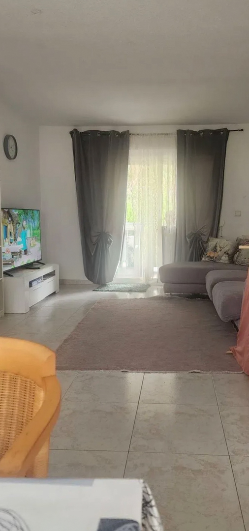Amplio salón con luz natural, suelos de baldosas, un cómodo sofá seccional y acceso directo a una terraza a través de puertas de cristal con cortinas elegantes.