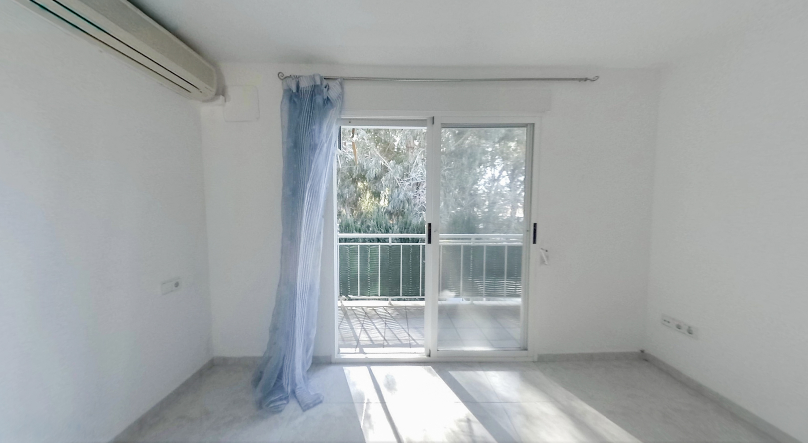 Dormitorio luminoso con aire acondicionado y acceso directo a una terraza privada. Suelo de baldosas claras y vistas a la vegetación exterior.