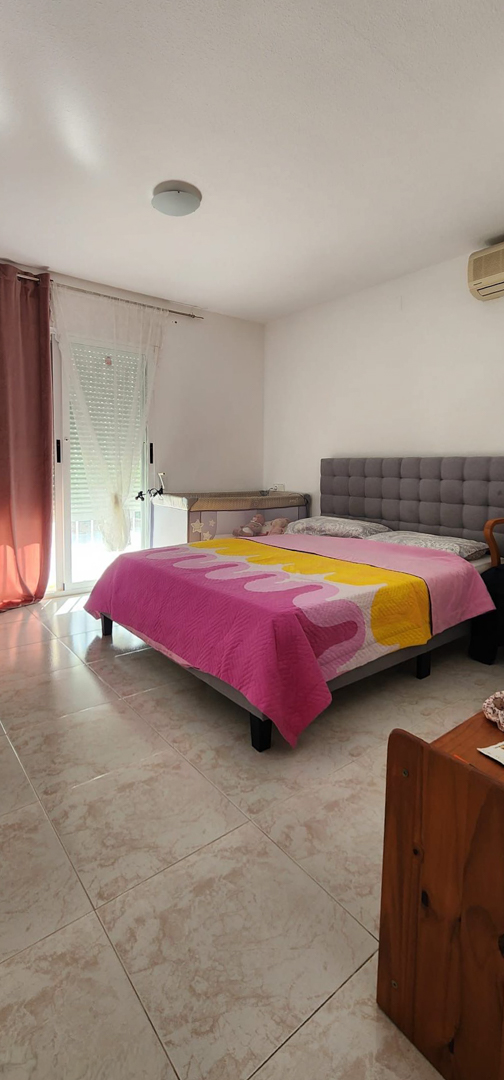 Dormitorio luminoso con cama doble, cabecero tapizado gris y suelo de gres. Cuenta con acceso a exterior y aire acondicionado.