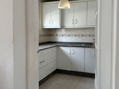 Cocina funcional con muebles blancos, encimeras de granito oscuro veteado y un salpicadero alicatado decorativo. La iluminación proviene de una lámpara colgante central y baldosas claras.