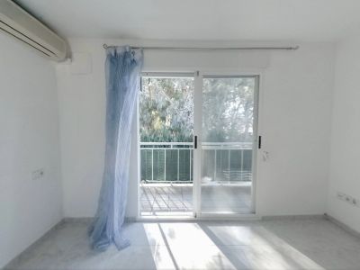 Dormitorio luminoso con aire acondicionado y acceso directo a una terraza privada. Suelo de baldosas claras y vistas a la vegetación exterior.