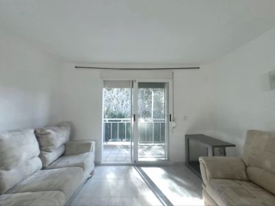 Luminoso salón con sofás claros, suelo de baldosas y puertas correderas de cristal que dan a un balcón, inundando el espacio con luz natural.