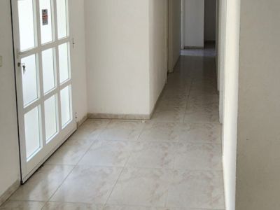 Vista del pasillo de entrada principal con suelo de baldosas claras, paredes blancas y una puerta con paneles de cristal. El corredor se extiende al interior, iluminado por un aplique de pared.